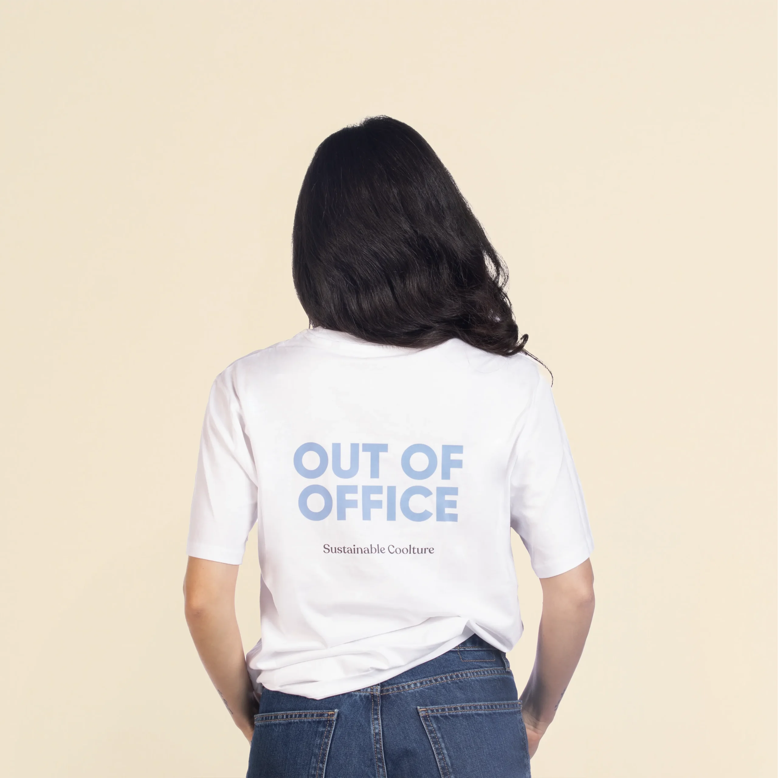 Chica morena de espaldas llevando jeans y una camiseta blanca personalizada con el texto 'out of office'