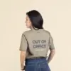 Chica morena de espaldas llevando jeans y una camiseta verde personalizada con el texto 'out of office'