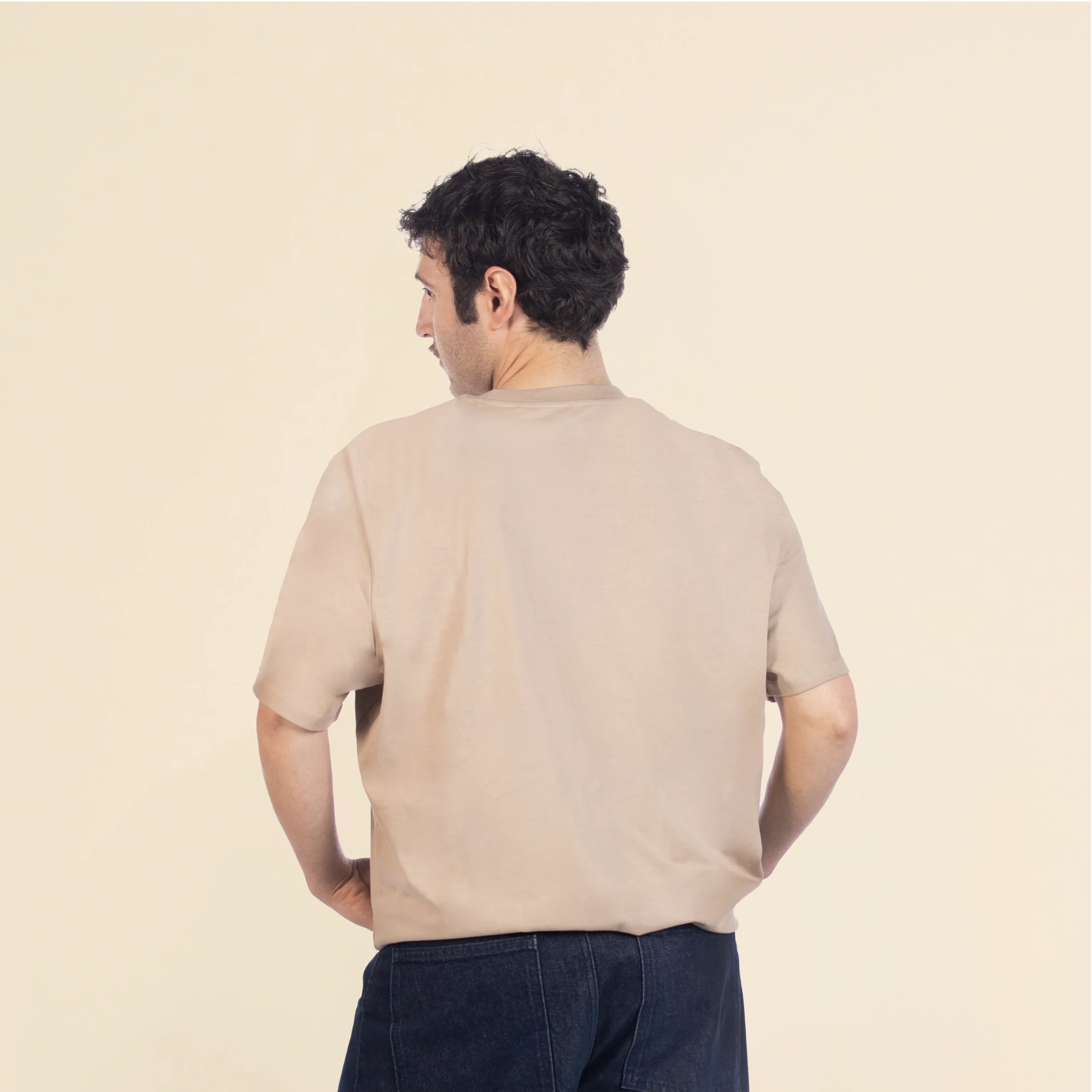Chico moreno de espaldas llevando jeans y una camiseta de algodón beige