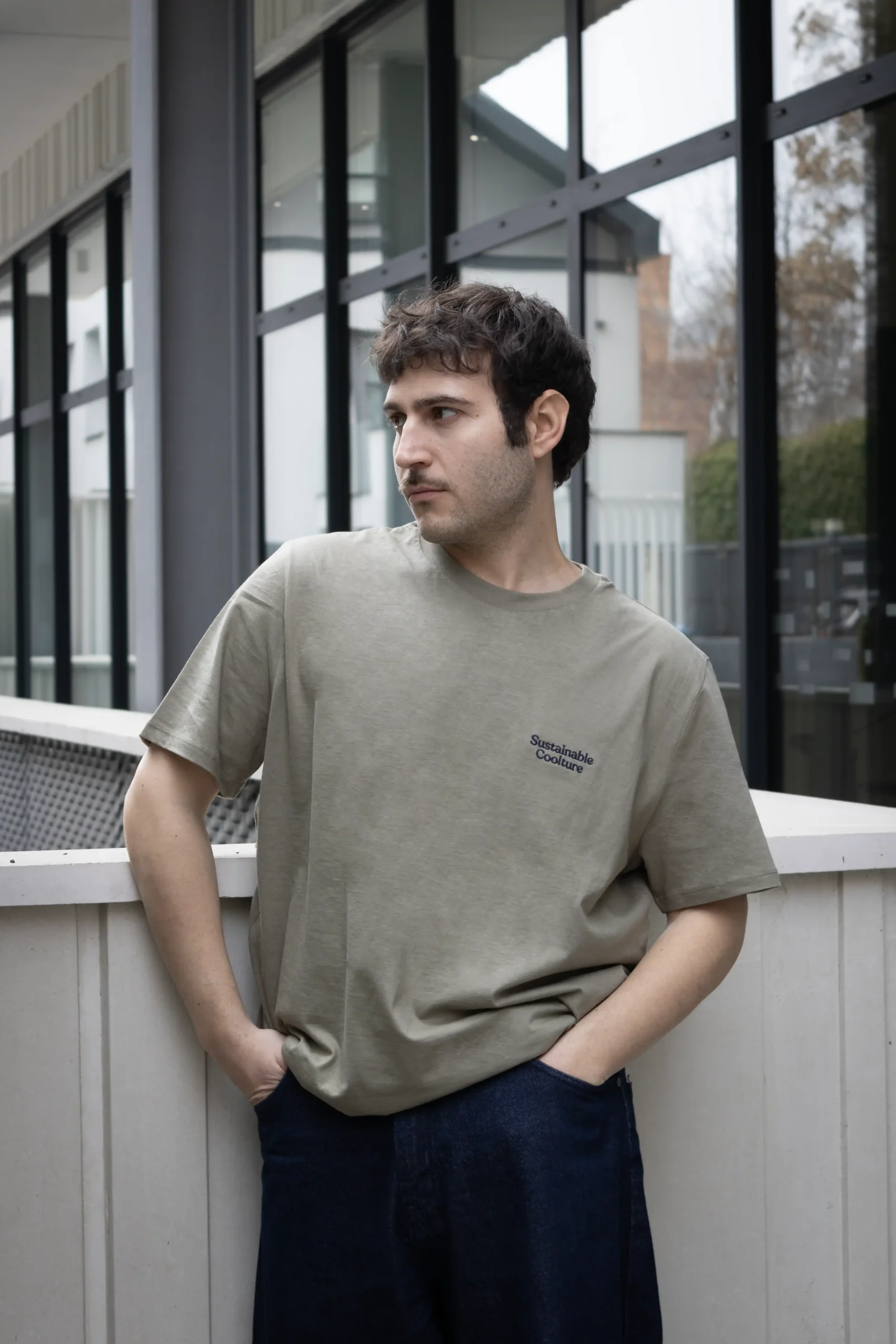 Chico moreno delante de un edificio llevando jeans y una camiseta verde personalizada