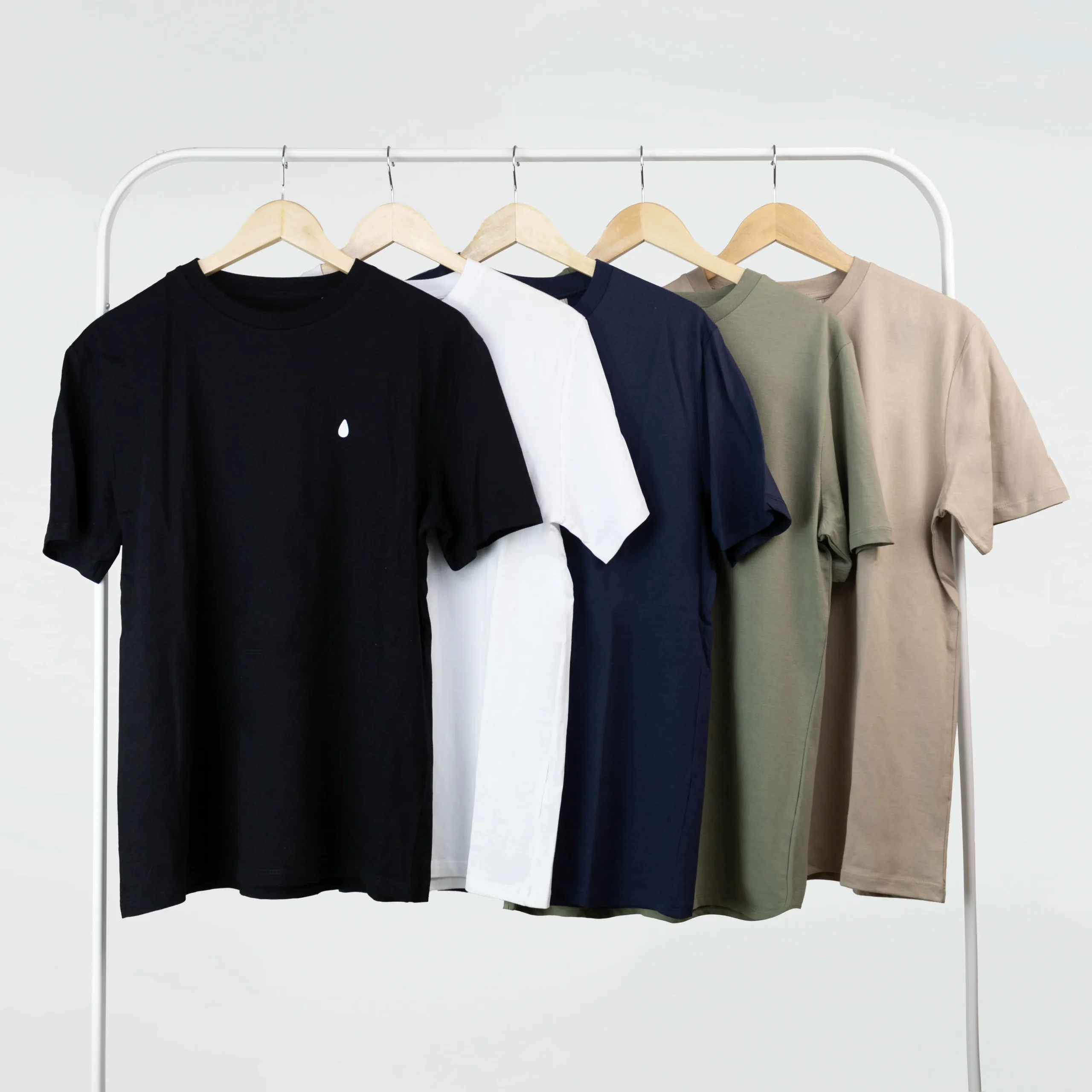 Cinco camisetas personalizadas de diferentes colores colgadas en perchas en un burro de ropa blanco