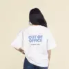 Camiseta oversize VEGA Blanca Chica morena de espaldas llevando jeans y una camiseta oversize blanca personalizada con el texto 'out of office'