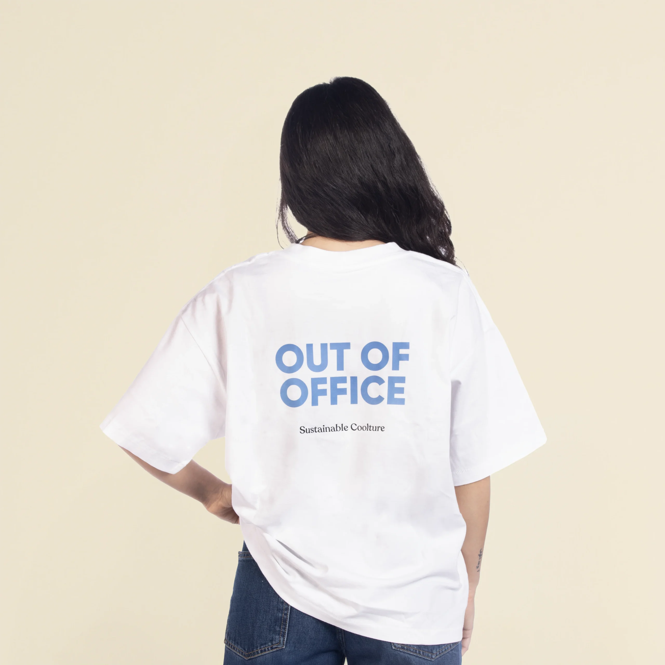 Camiseta oversize VEGA Blanca Chica morena de espaldas llevando jeans y una camiseta oversize blanca personalizada con el texto 'out of office'