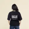 Camiseta oversize VEGA Negra Chica morena de espaldas llevando jeans y una camiseta oversize negra personalizada con el texto 'out of office'