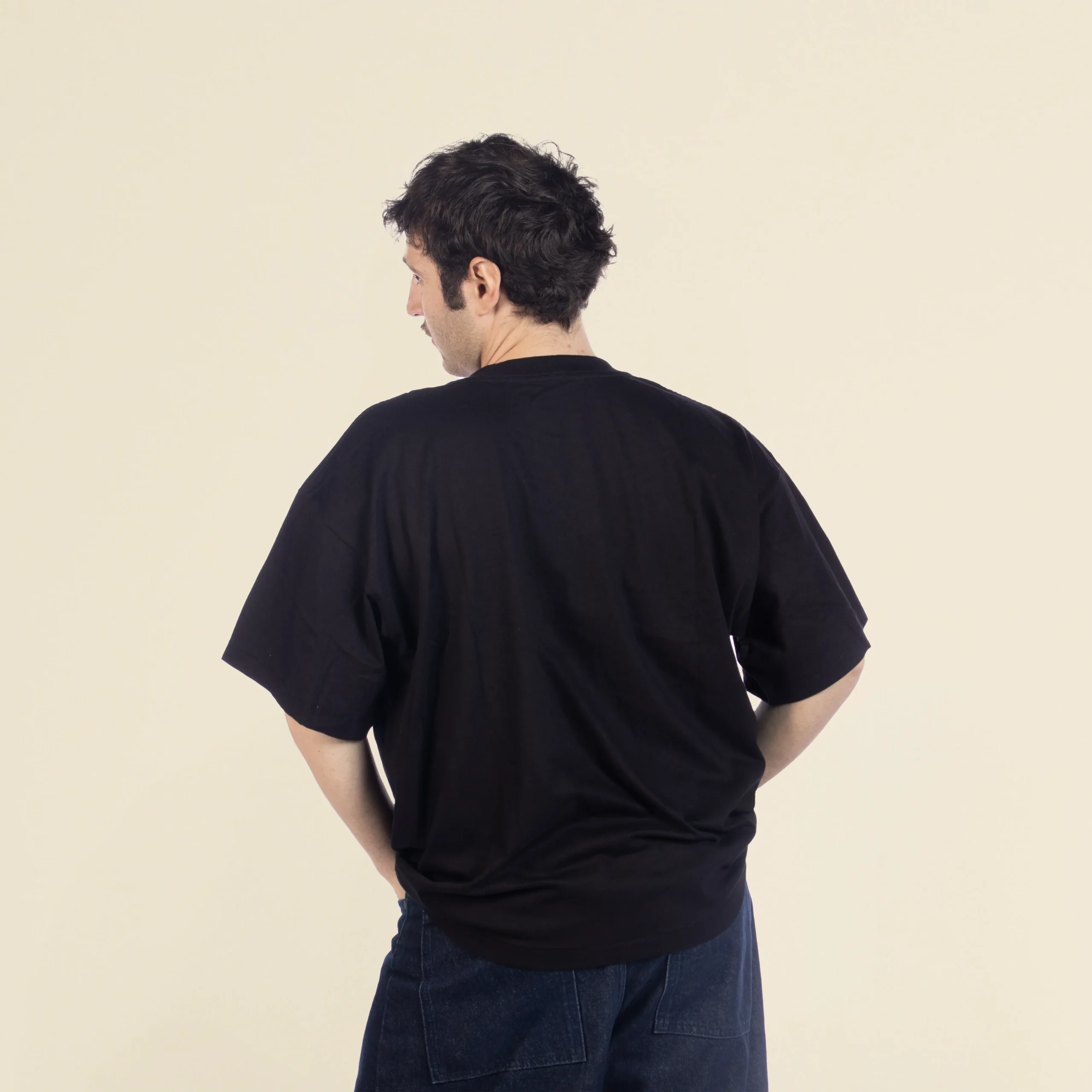 Camiseta oversize VEGA Negra Chico moreno de espaldas llevando jeans y una camiseta oversize negra