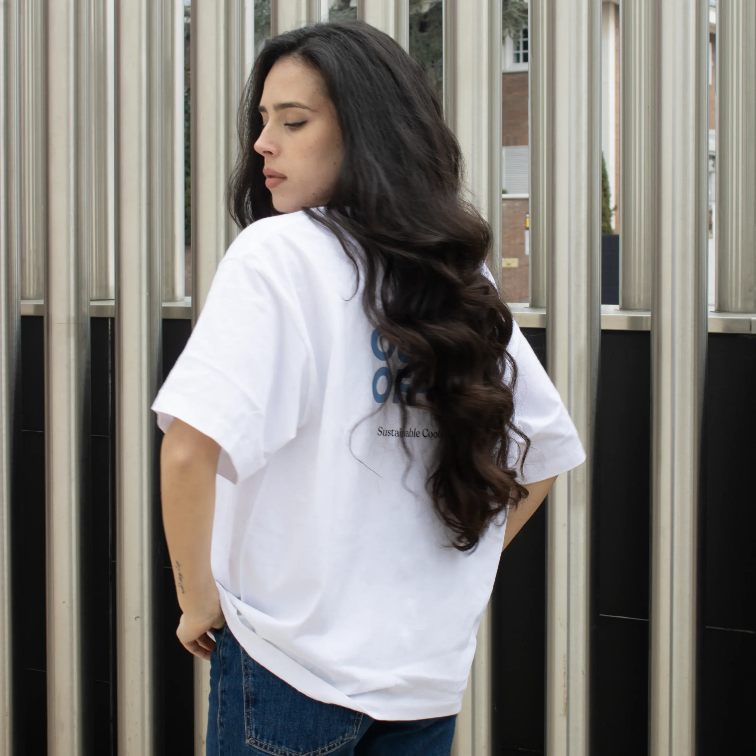 Une jeune femme brune, de dos, portant un jean et un t-shirt oversize blanc personnalisé