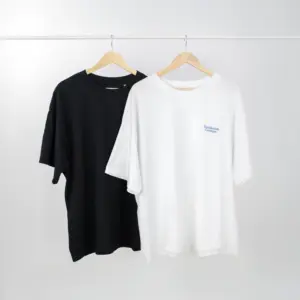 Una camiseta negra y una camiseta blanca colgadas en perchas de una barra blanca