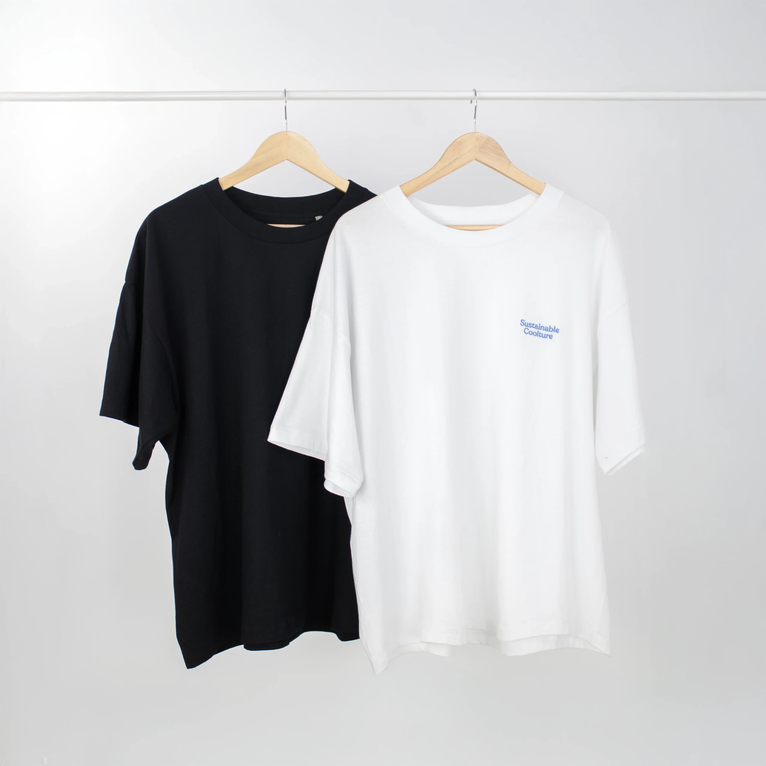 Una camiseta negra y una camiseta blanca colgadas en perchas de una barra blanca