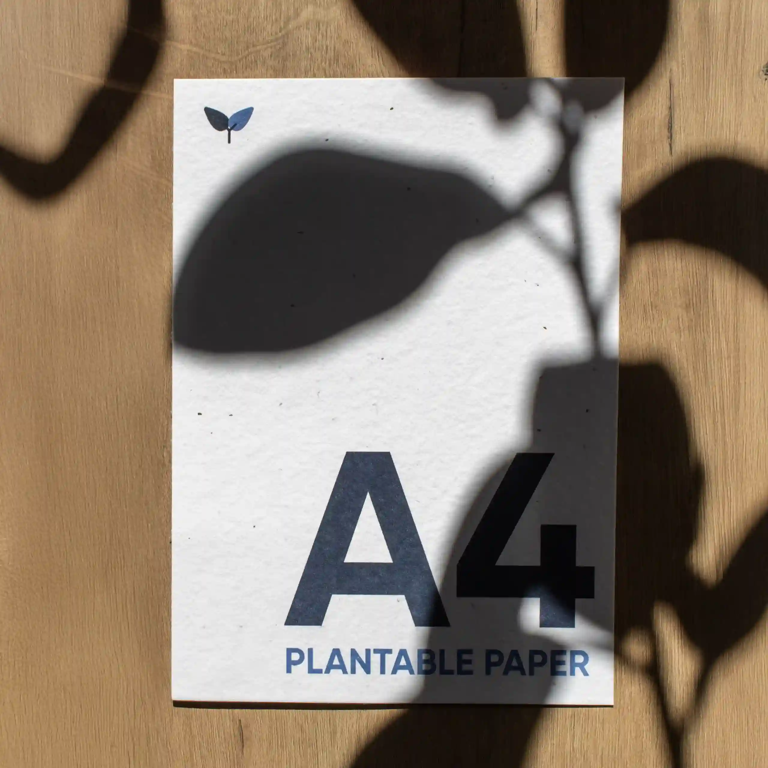 Hoja A5 impresa en papel plantable sobre una superficie de madera con sombras