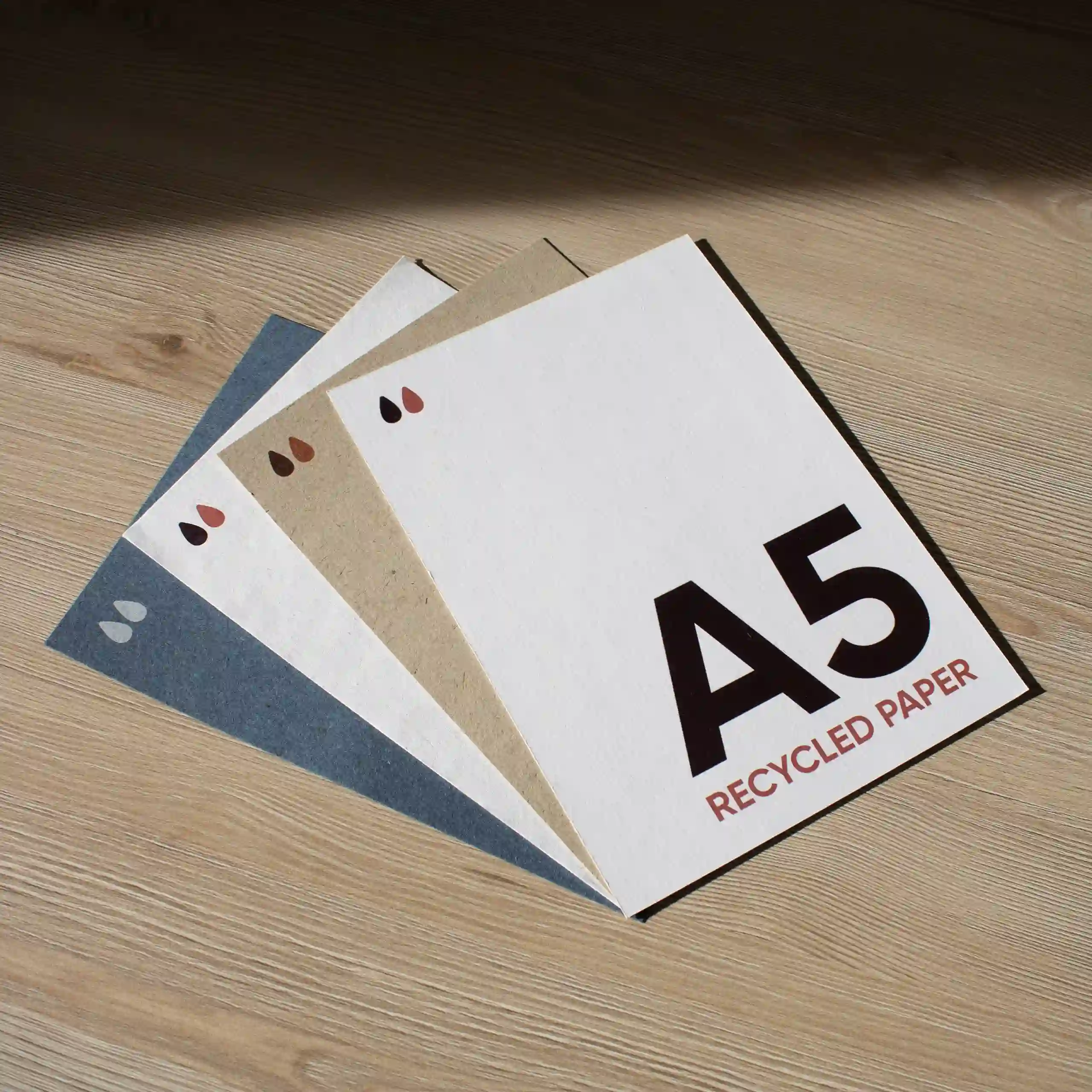 cuatro tarjetas A5 impresas en papeles ecológicos sobre una superficie de madera