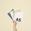 Mano sujetando cuatro tarjetas A5 impresas en papeles ecológicos