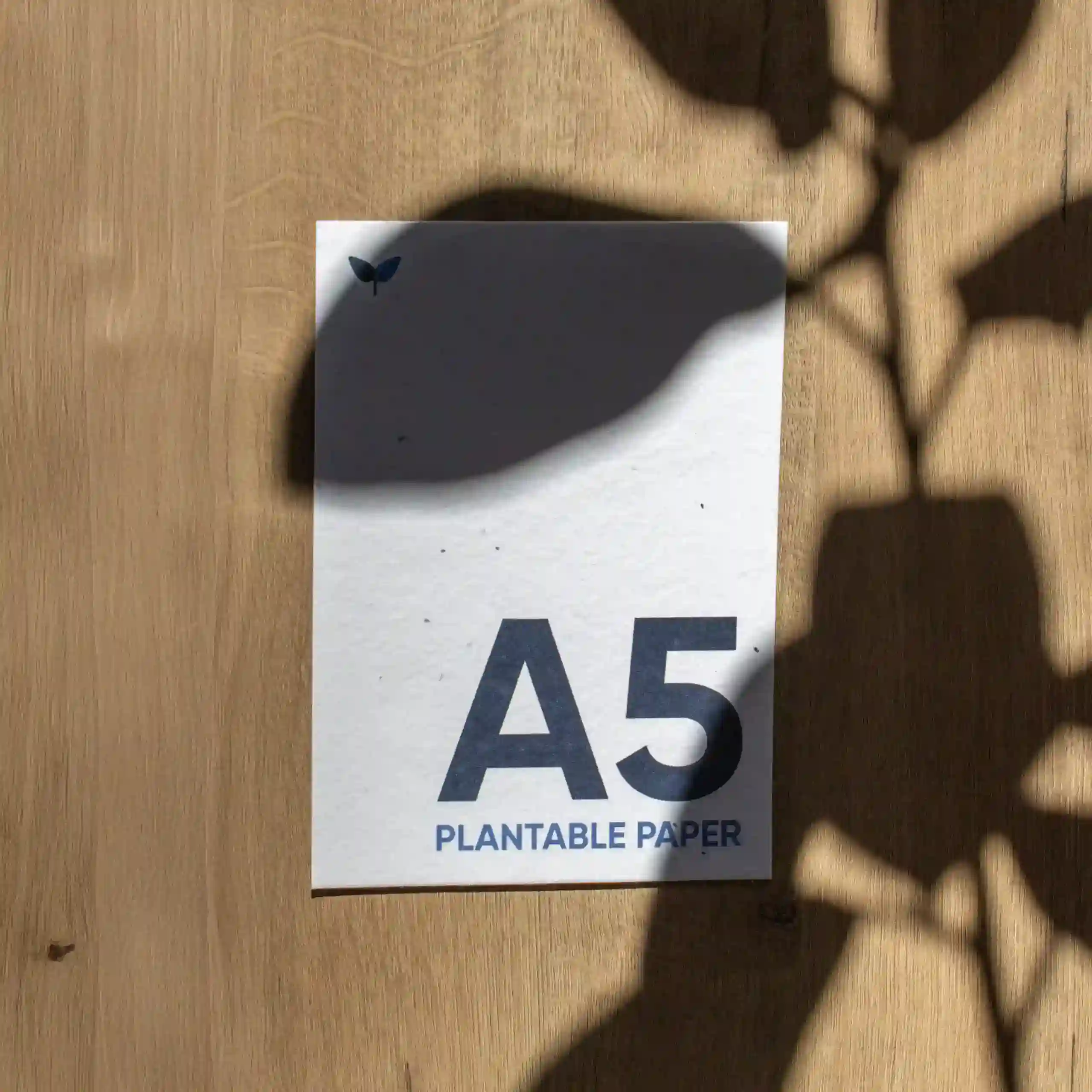 Tarjeta A5 impresa en papel plantable sobre una superficie de madera con sombras
