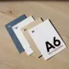 cuatro tarjetas A6 impresas en papeles ecológicos sobre una superficie de madera