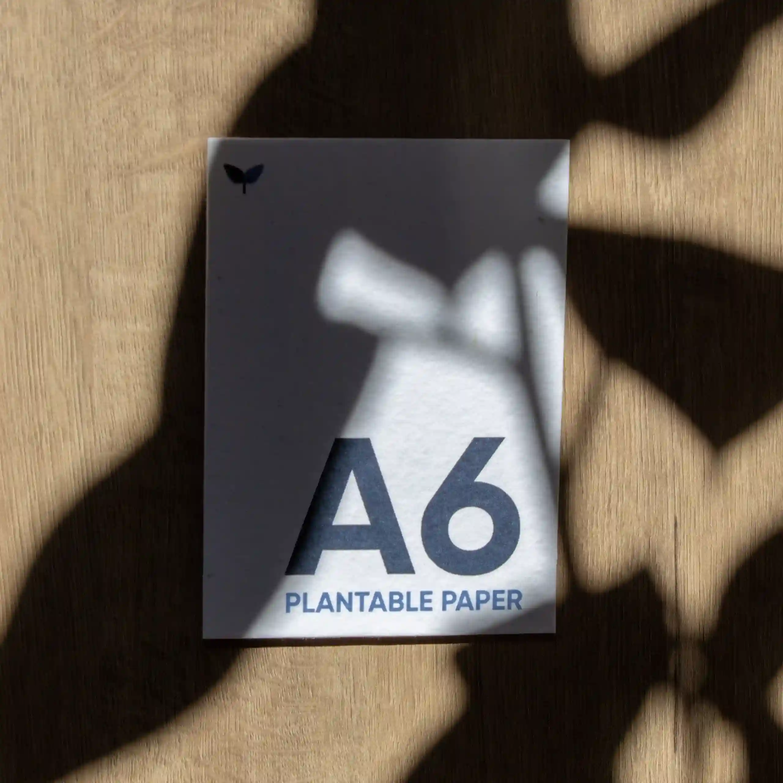 Tarjeta A6 impresa en papel plantable sobre una superficie de madera con sombras