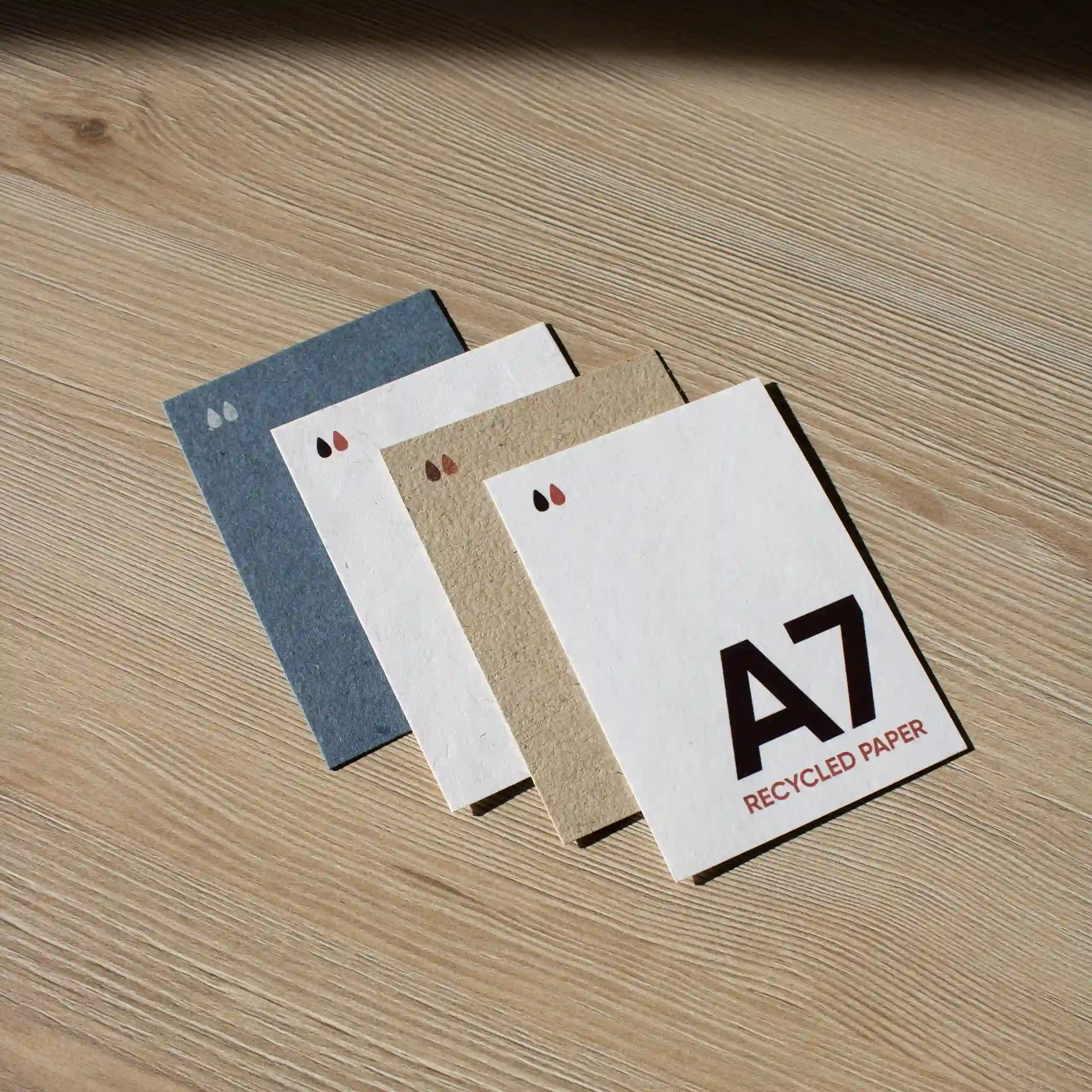 Cuatro tarjetas A7 impresas en papeles ecológicos sobre una superficie de madera