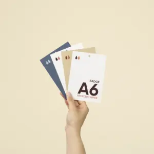 Mano sujetando cuatro acreditaciones A6 impresas en papeles ecológicos