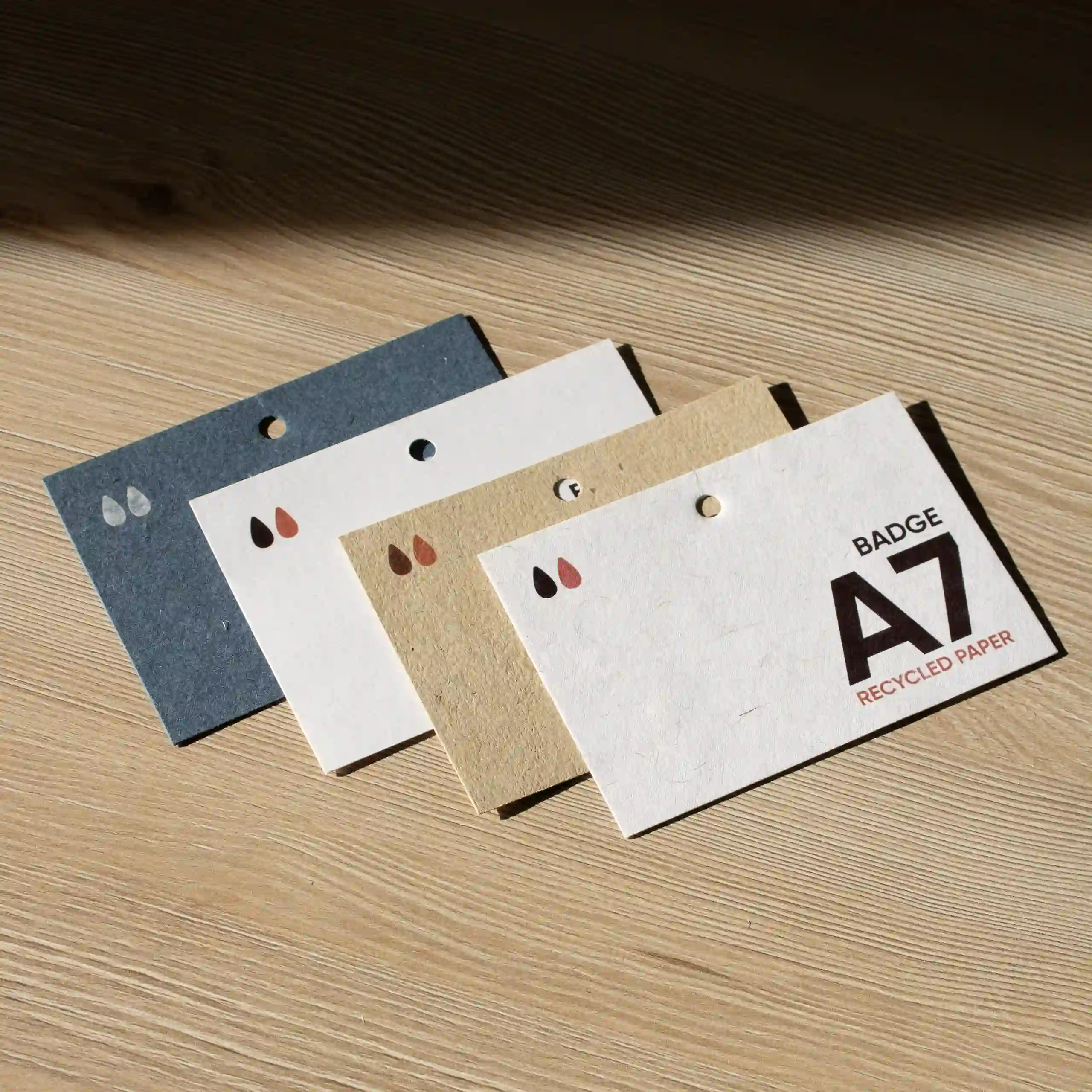 Cuatro acreditaciones A7 impresas en papeles ecológicos sobre superficie de madera