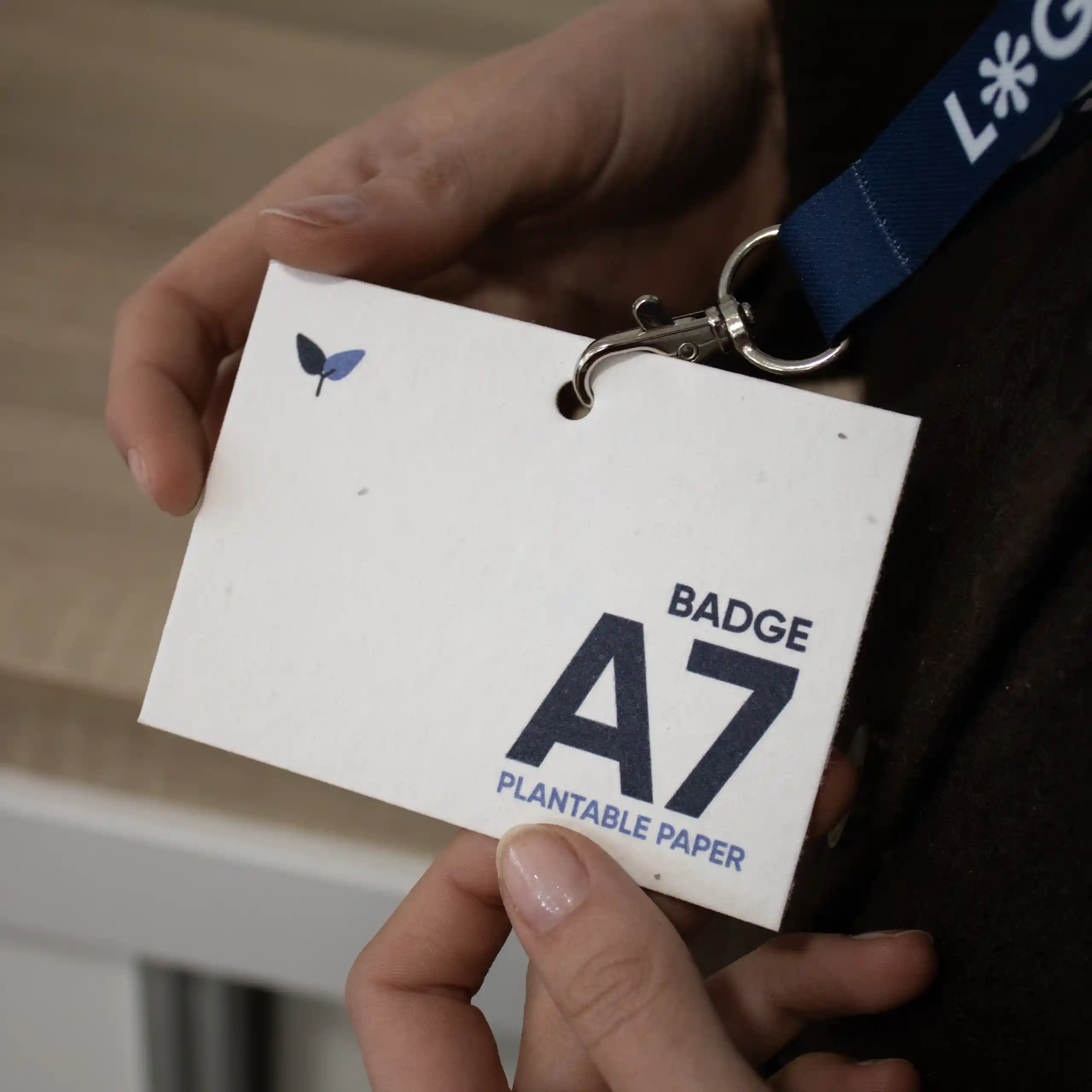 Manos sujetando una acreditación A7 impresa en papel plantable colgada de un lanyard