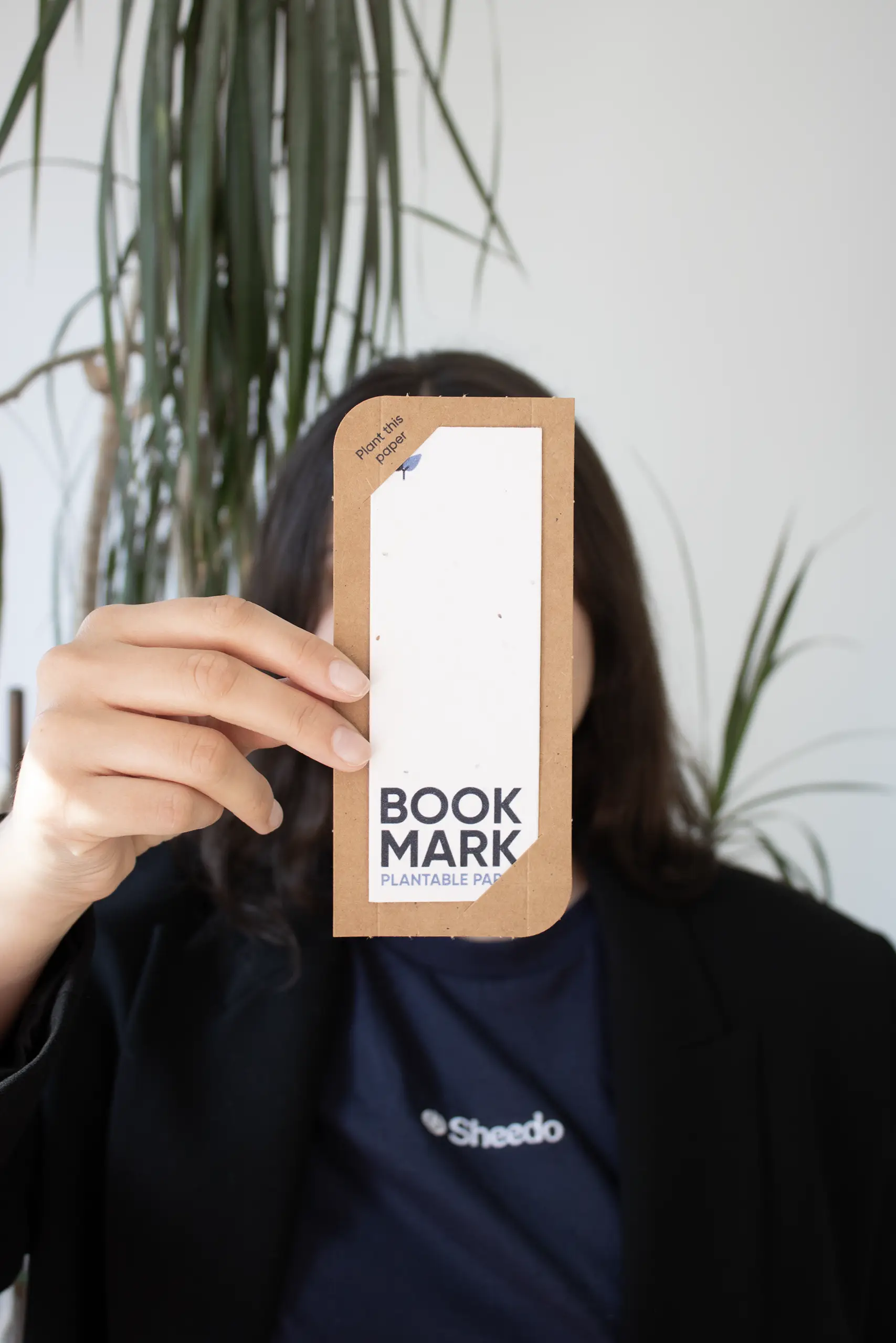 Chica mostrando a cámara un marcapáginas impreso en papel plantable dentro de una funda en cartón kraft