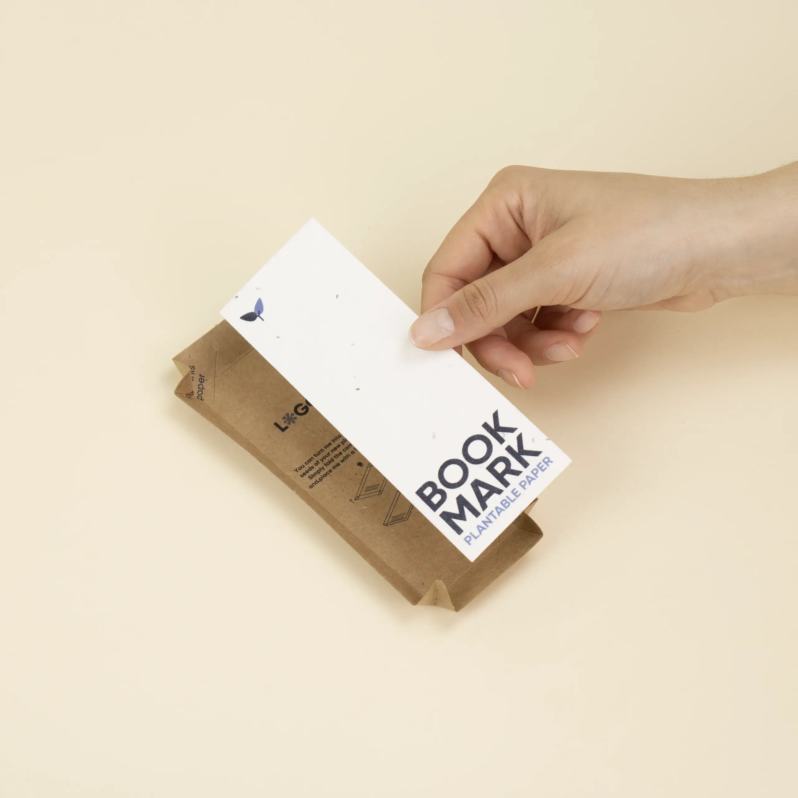 Mano colocando un marcapáginas de papel plantable sobre un recipiente hecho de cartón kraft