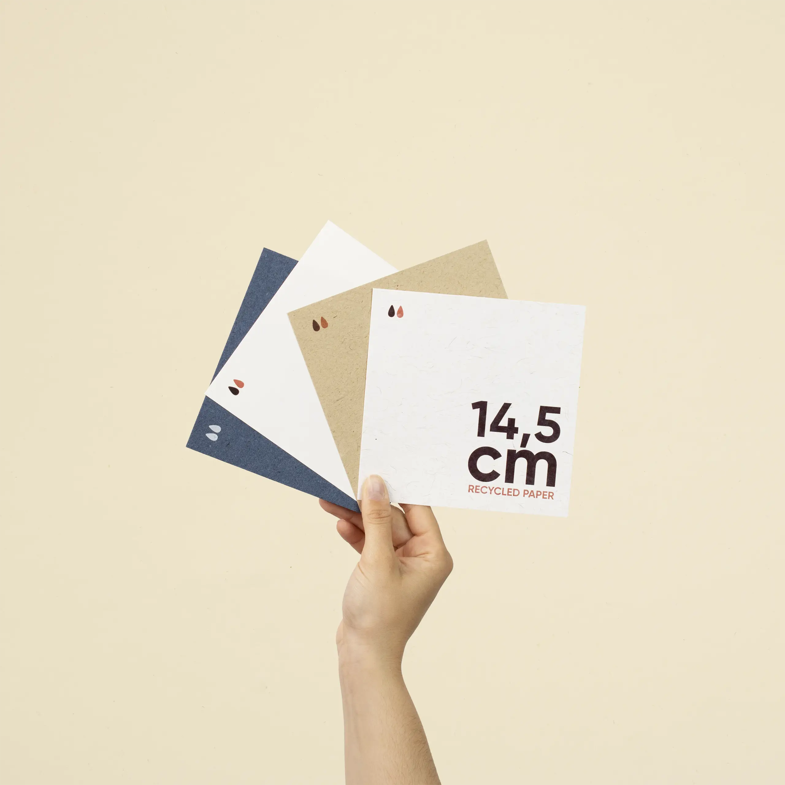 Mano sujetando cuatro tarjetas cuadradas impresas en papel ecológico
