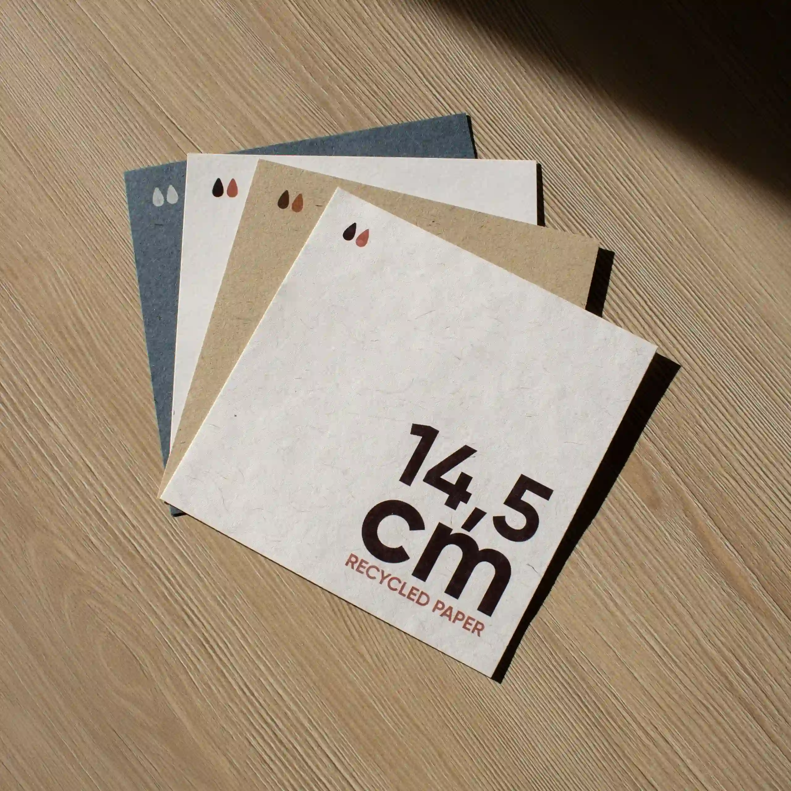 Cuatro tarjetas cuadradas impresas en papel ecológico sobre una superficie de madera