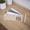 Tarjeta papel ecológico DL Cuatro tarjetas DL impresas en papel ecológico junto a un bolígrafo sobre una superficie de madera
