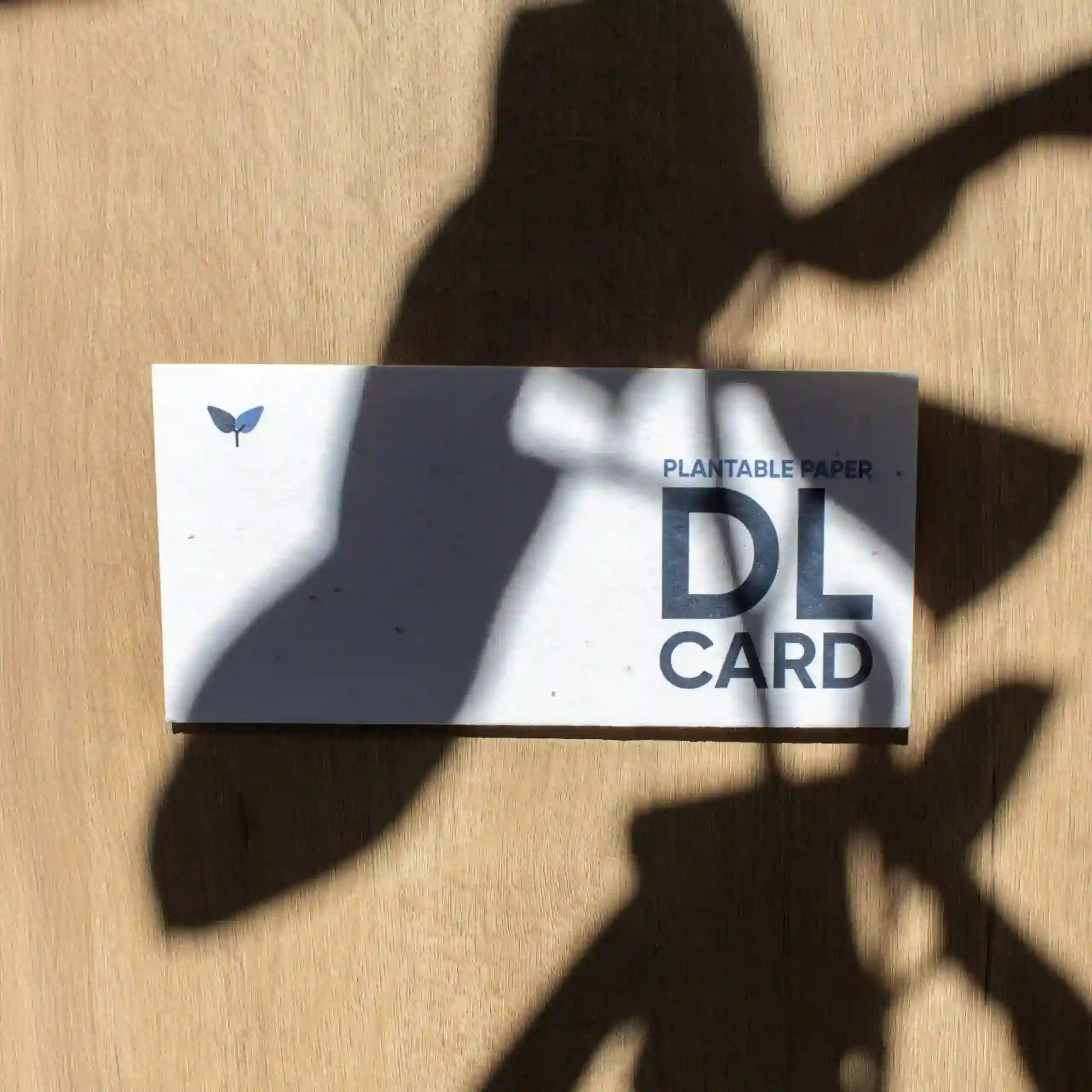 Tarjeta DL impresa en papel plantable sobre una superficie de madera con sombras