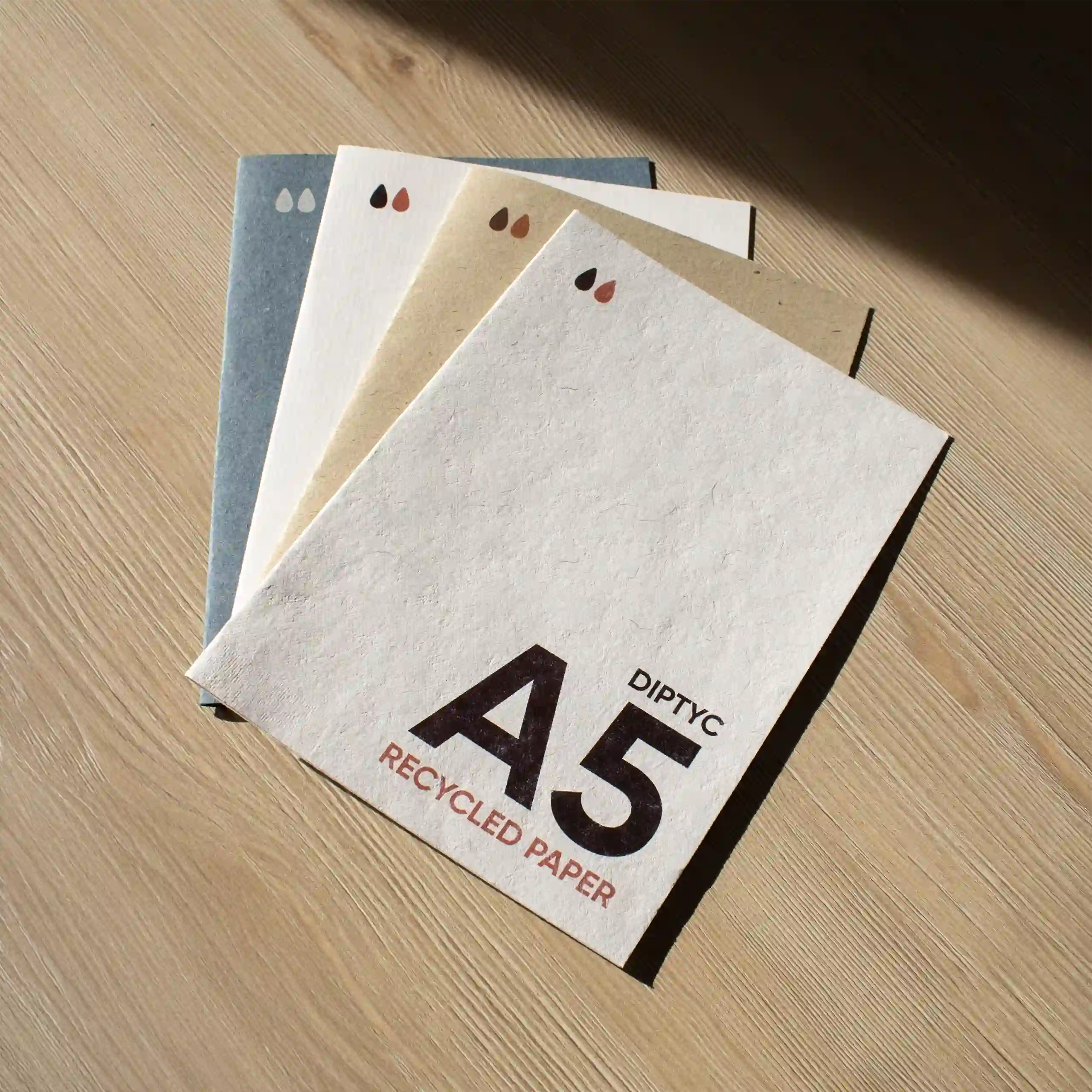 Cuatro dípticos A5 impresos en papel ecológico sobre una superficie de madera