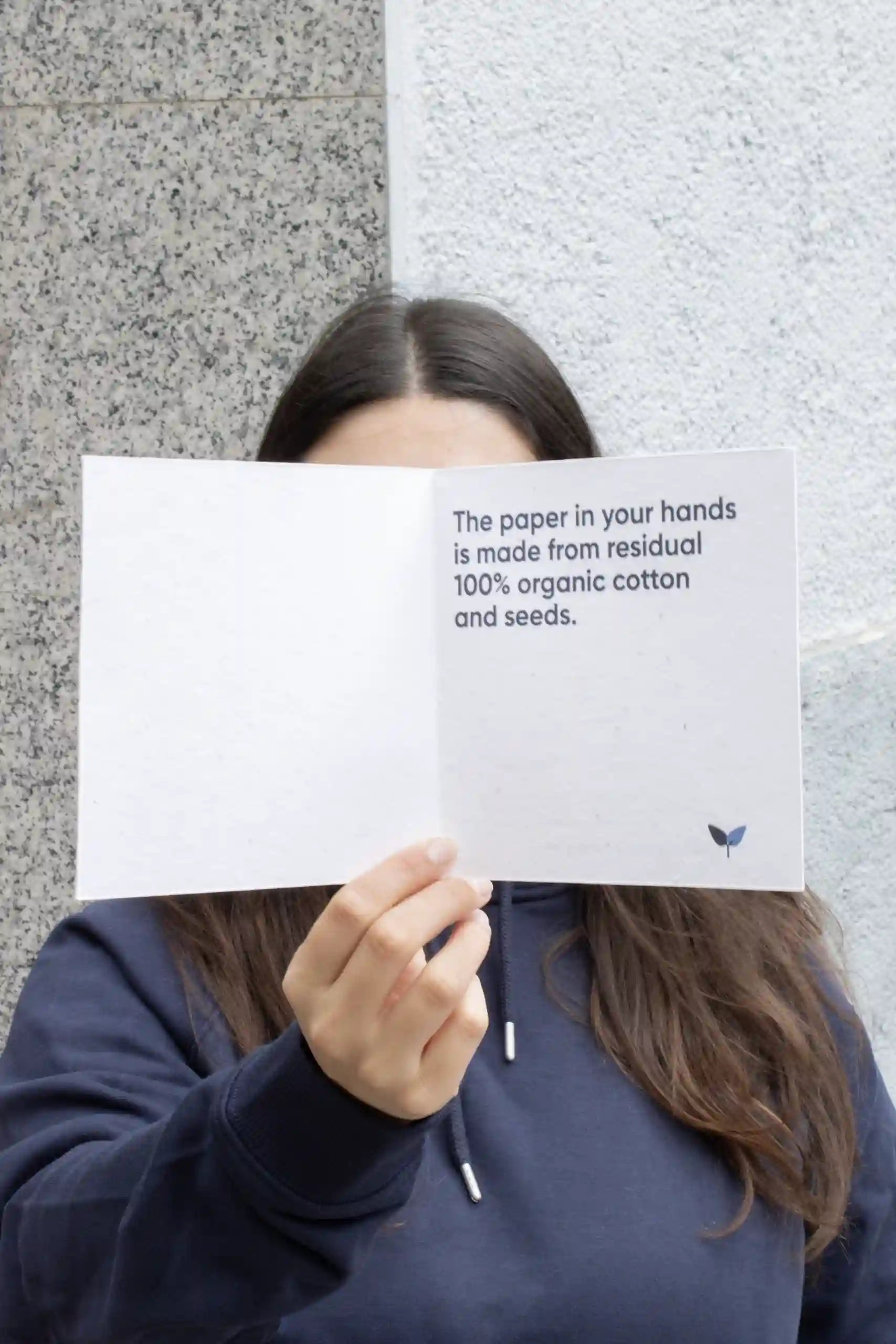 Chica mostrando a cámara un díptico cuadrado impreso en papel plantable