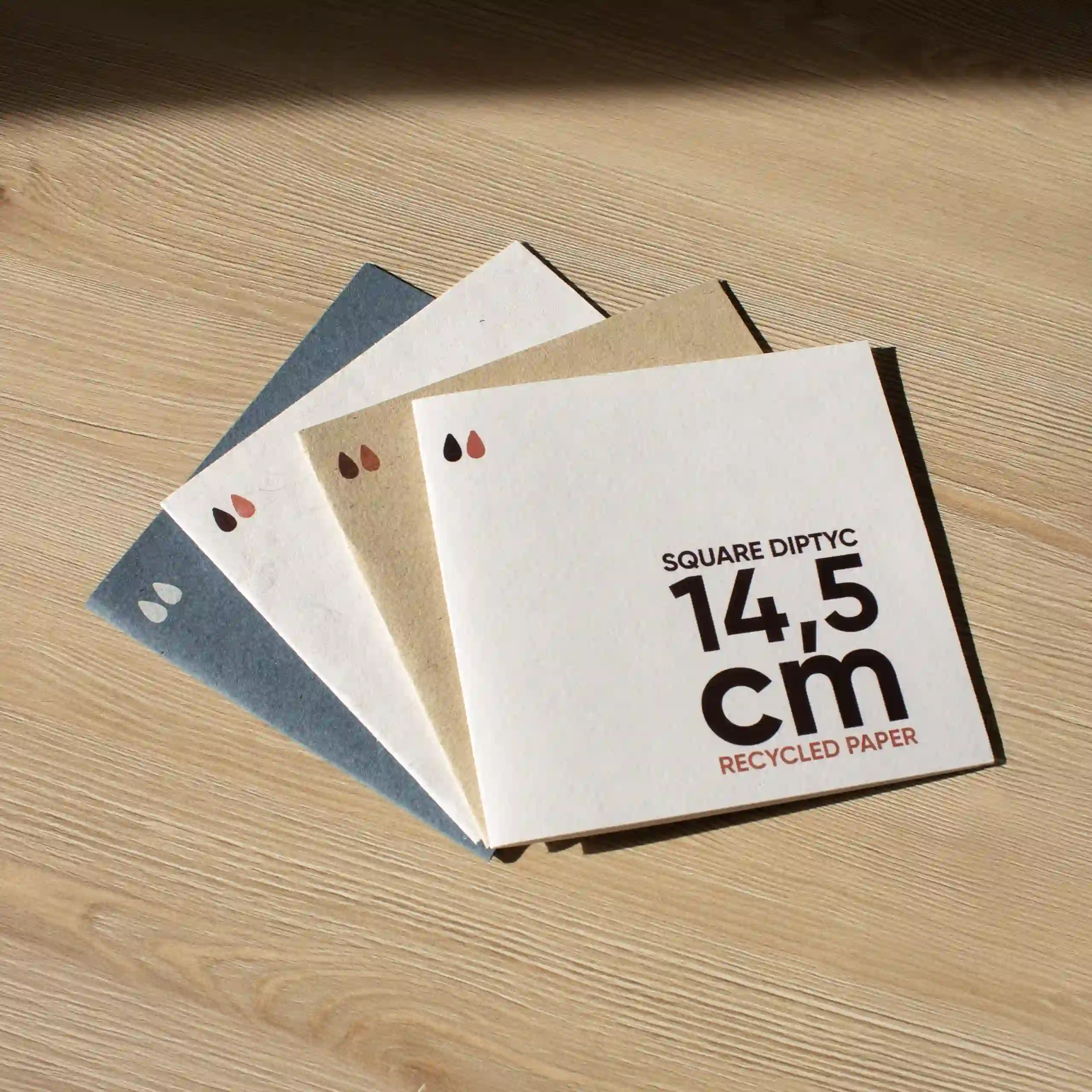 Cuatro dípticos cuadrados impresos en papel ecológico sobre un superficie de madera