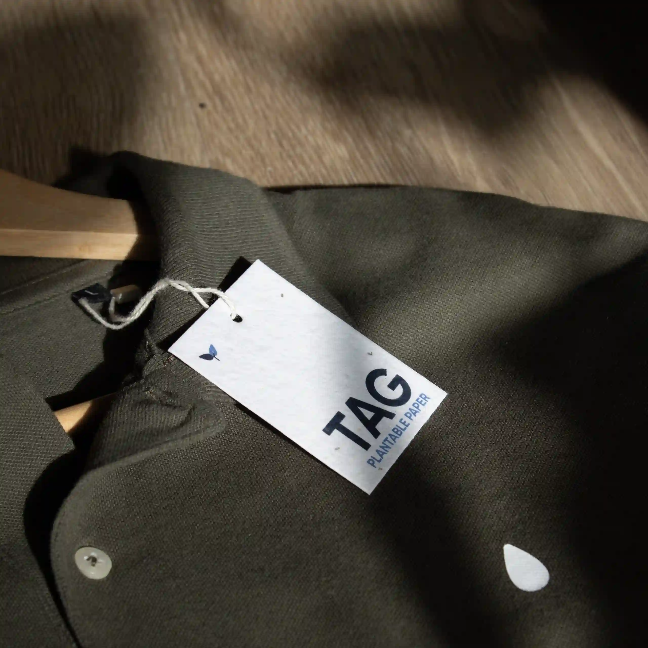 Una etiqueta de ropa impresa en papel plantable colgada de un polo verde colocado sobre una superficie de madera