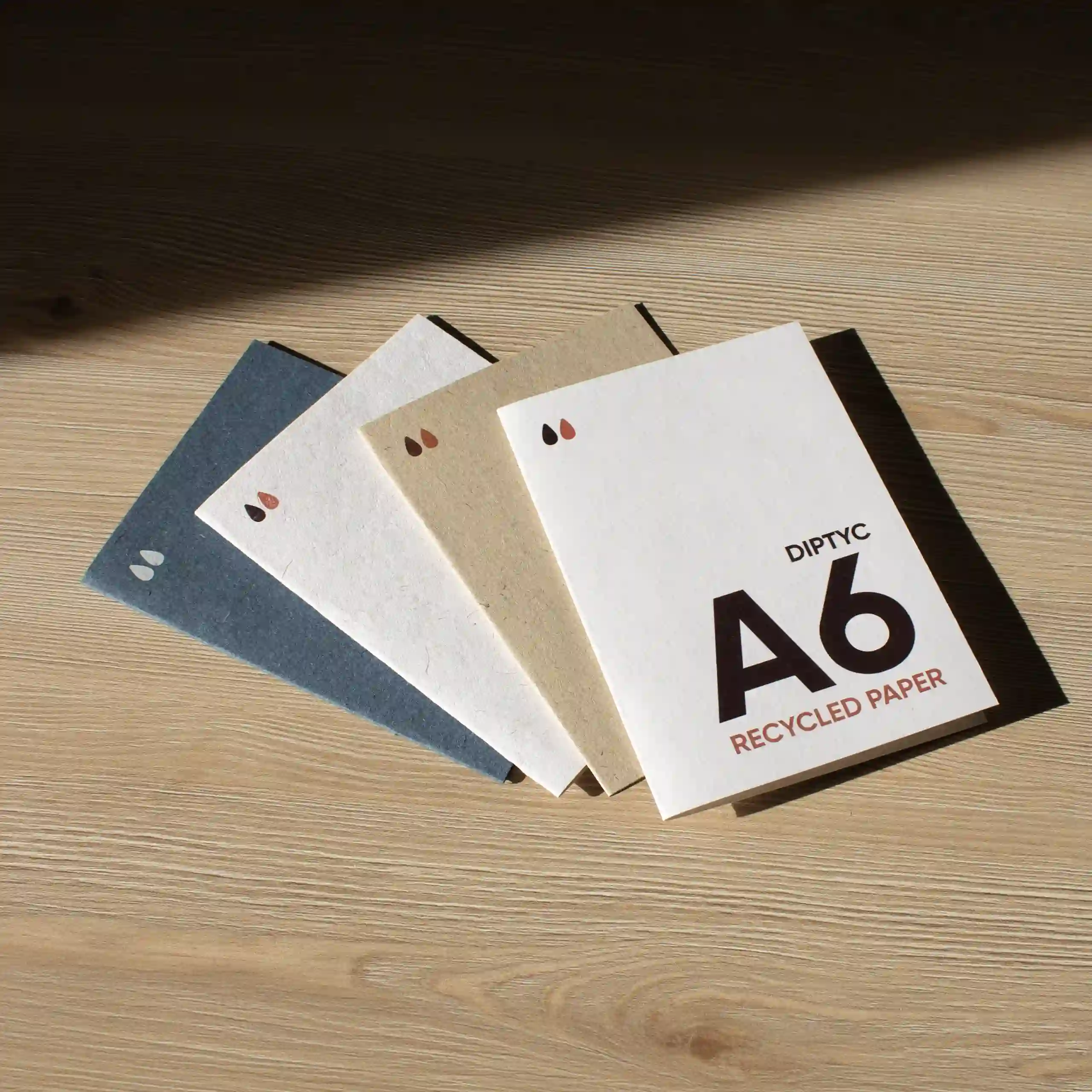 Cuatro dípticos A6 impresos en papel ecológico sobre una superficie de madera