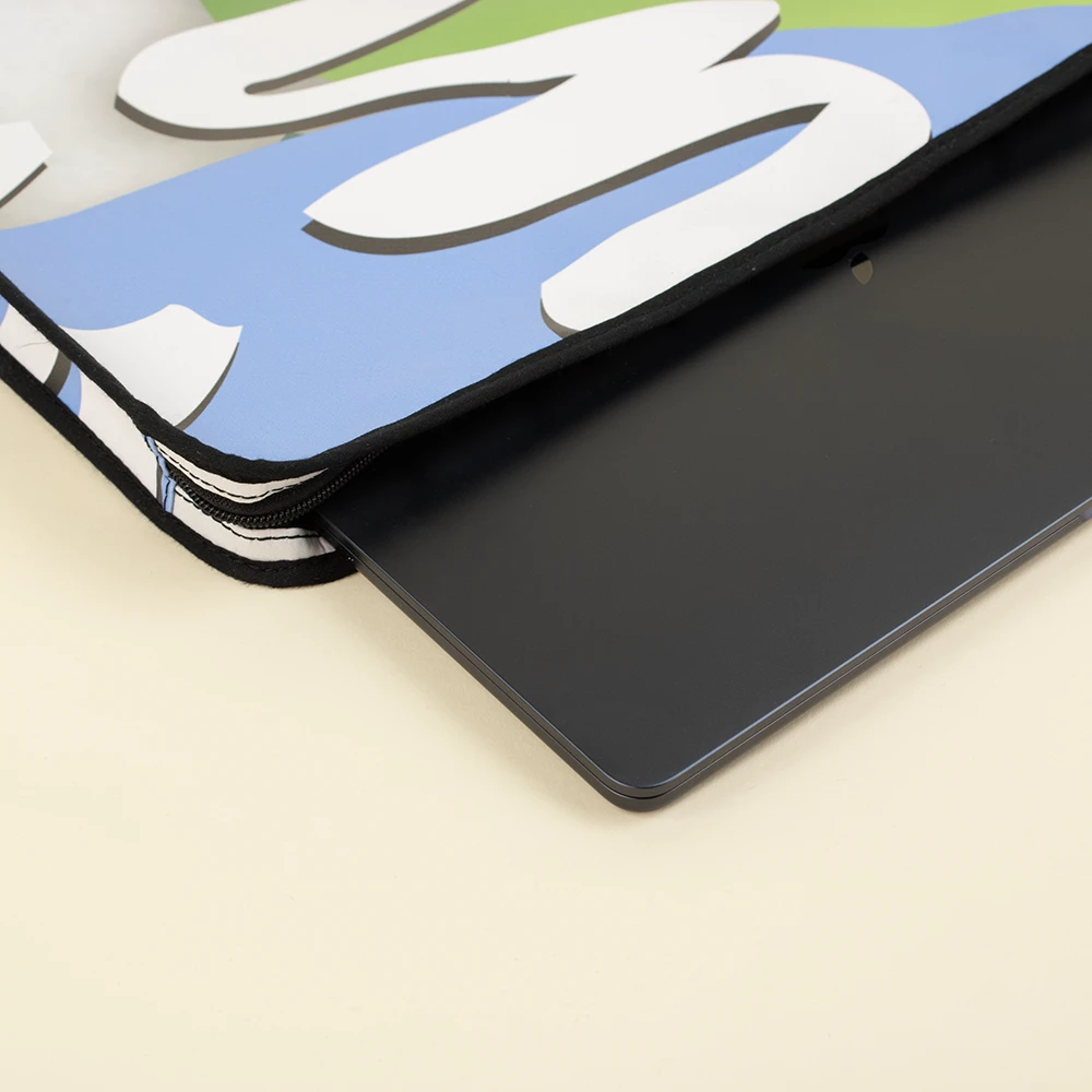 Funda de portátil personalizada hecha con lona reciclada abierta junto a un portátil de color negro