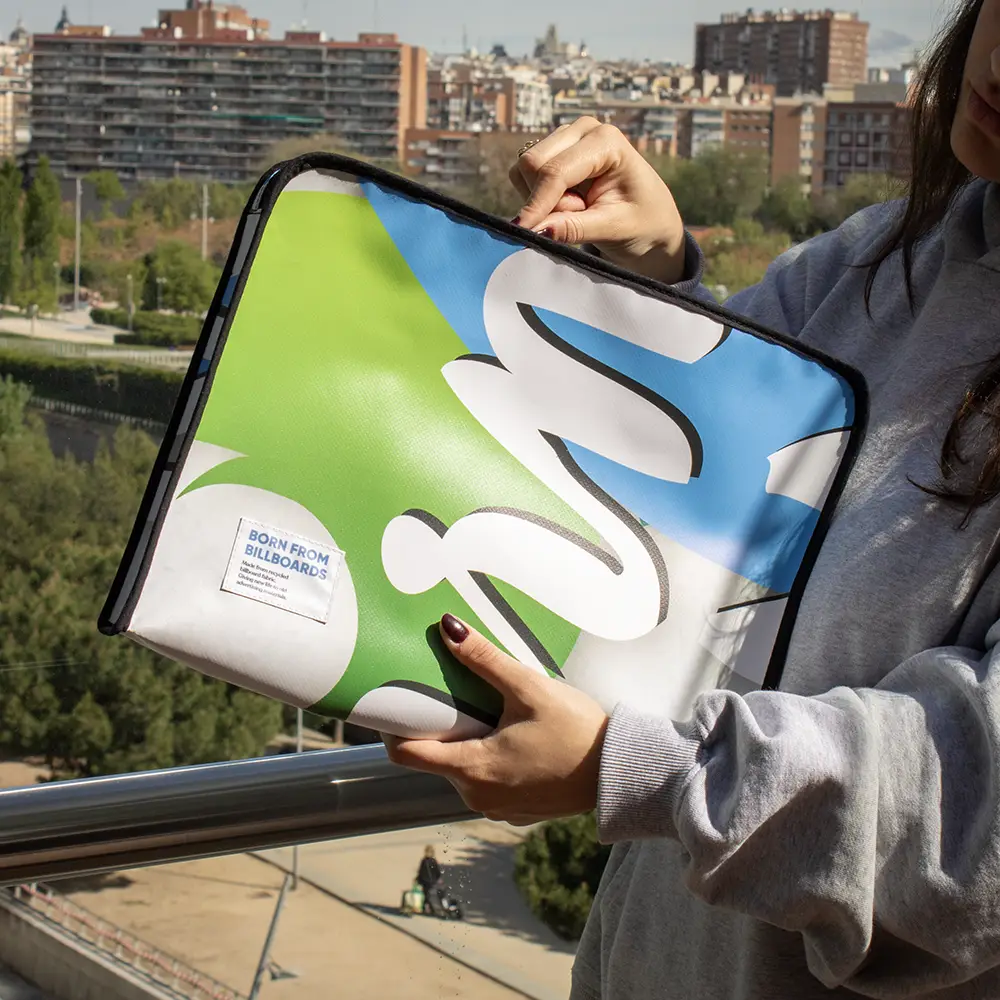 Chica en la calle abriendo una funda de portátil personalizada hecha con lona reciclada, con la ciudad de fondo