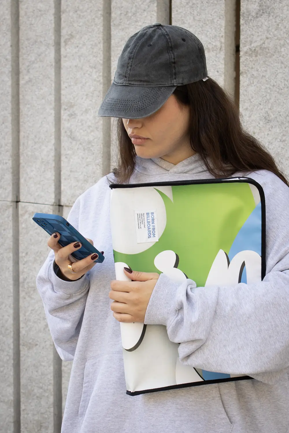 Chica en la calle mirando el móvil y llevando una funda de portátil personalizada hecha con lona reciclada