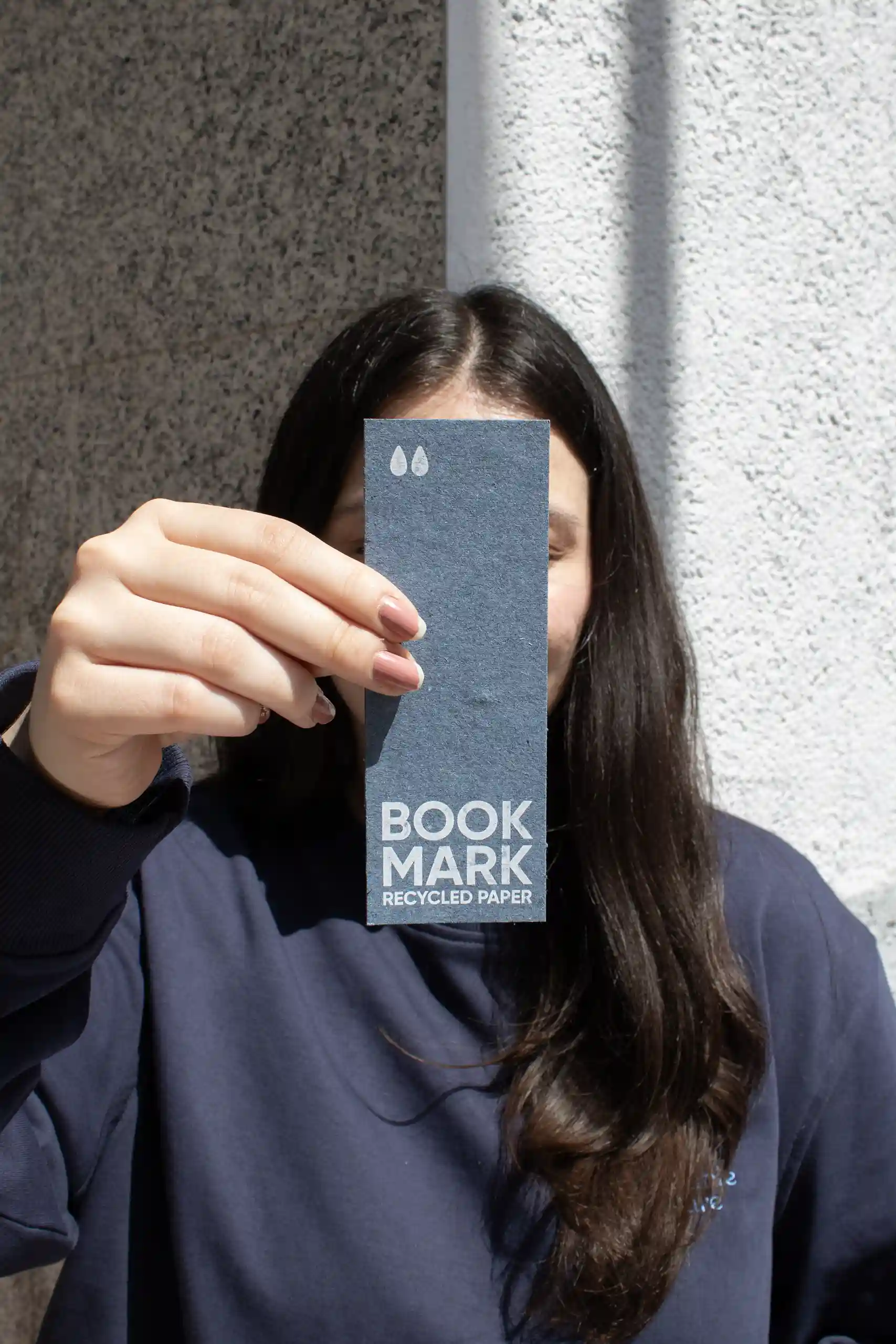 Chica mostrando a cámara un marcapáginas de papel ecológico