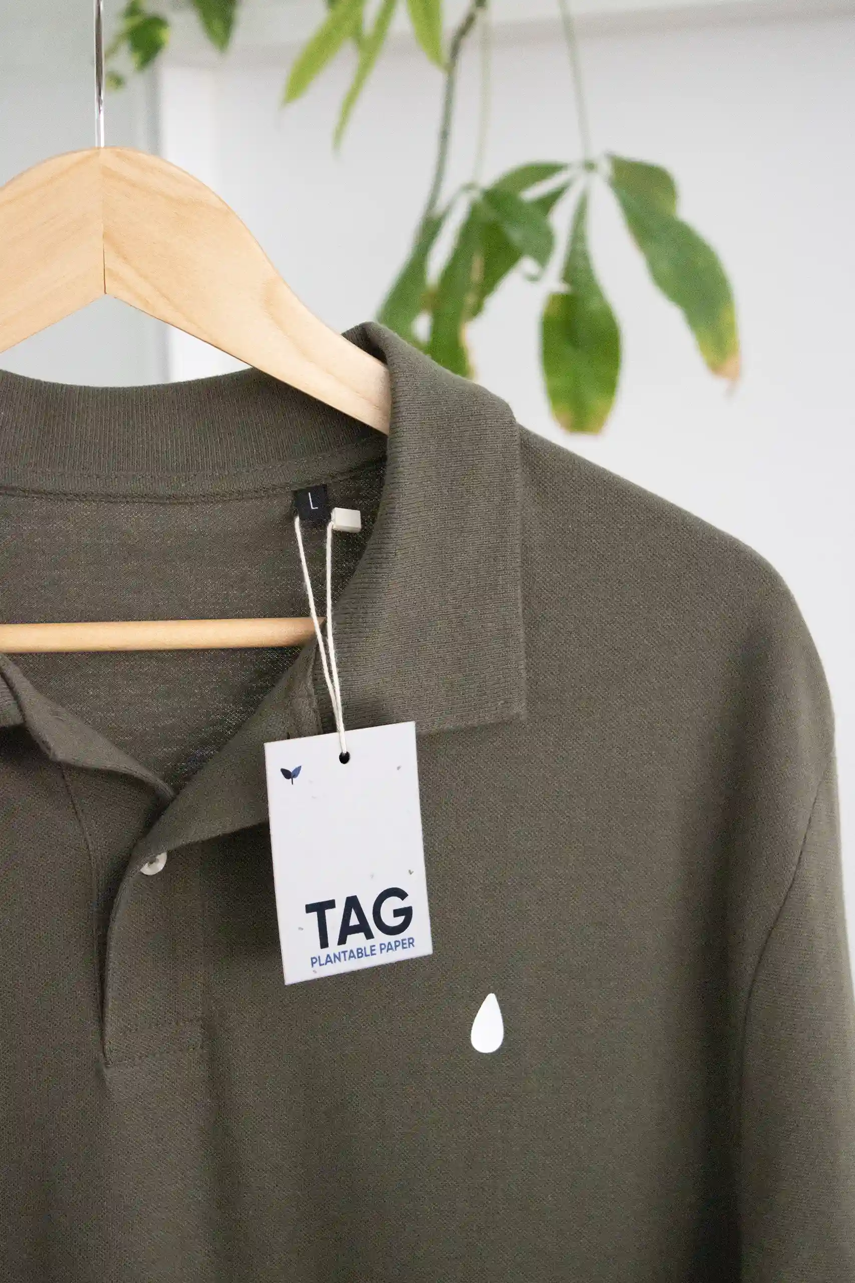 Etiqueta impresa en papel plantable con un marchamo biodegradable blanco colgada de una camiseta verde perchada