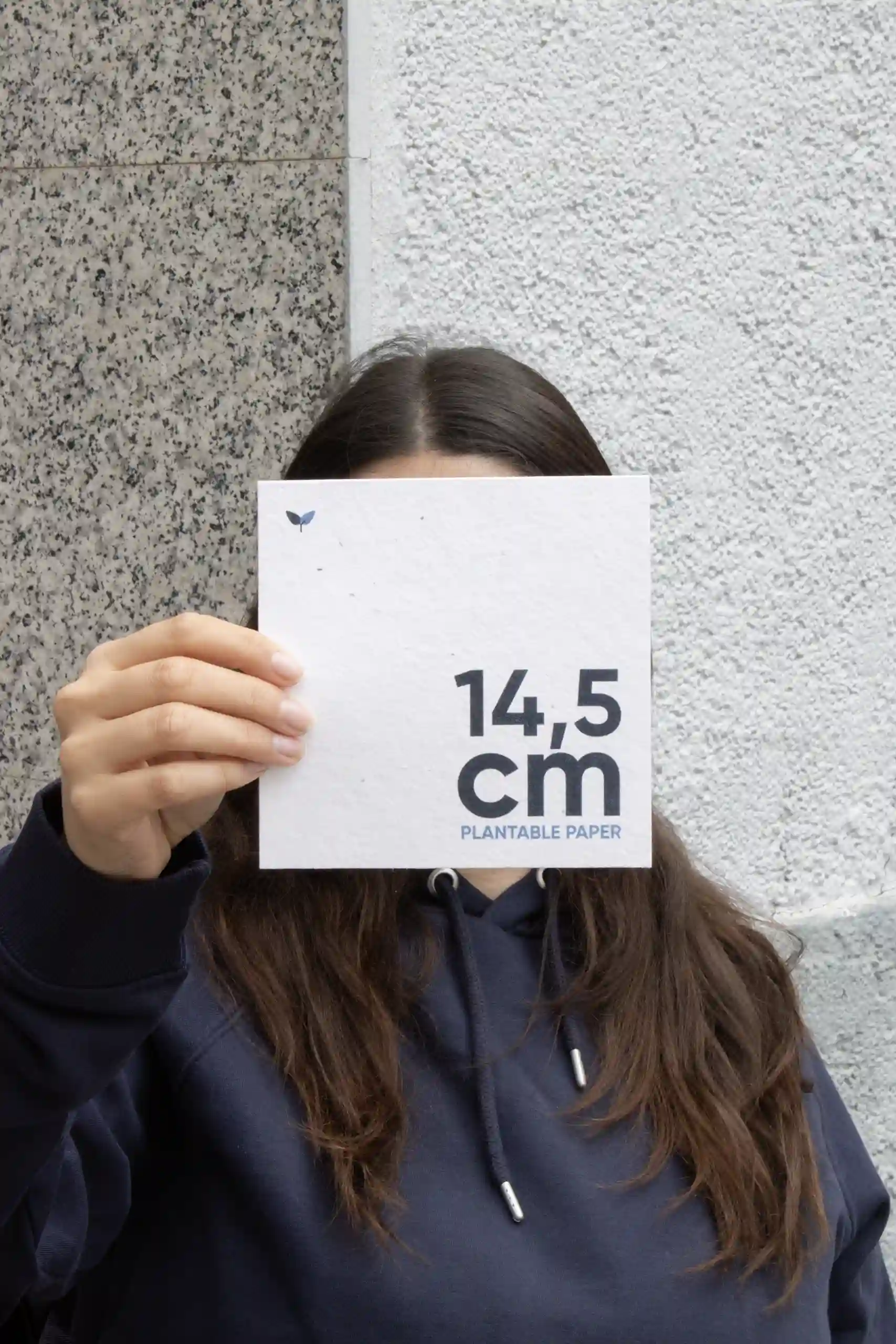 Chica mostrando a cámara una tarjeta cuadrada impresa en papel plantable