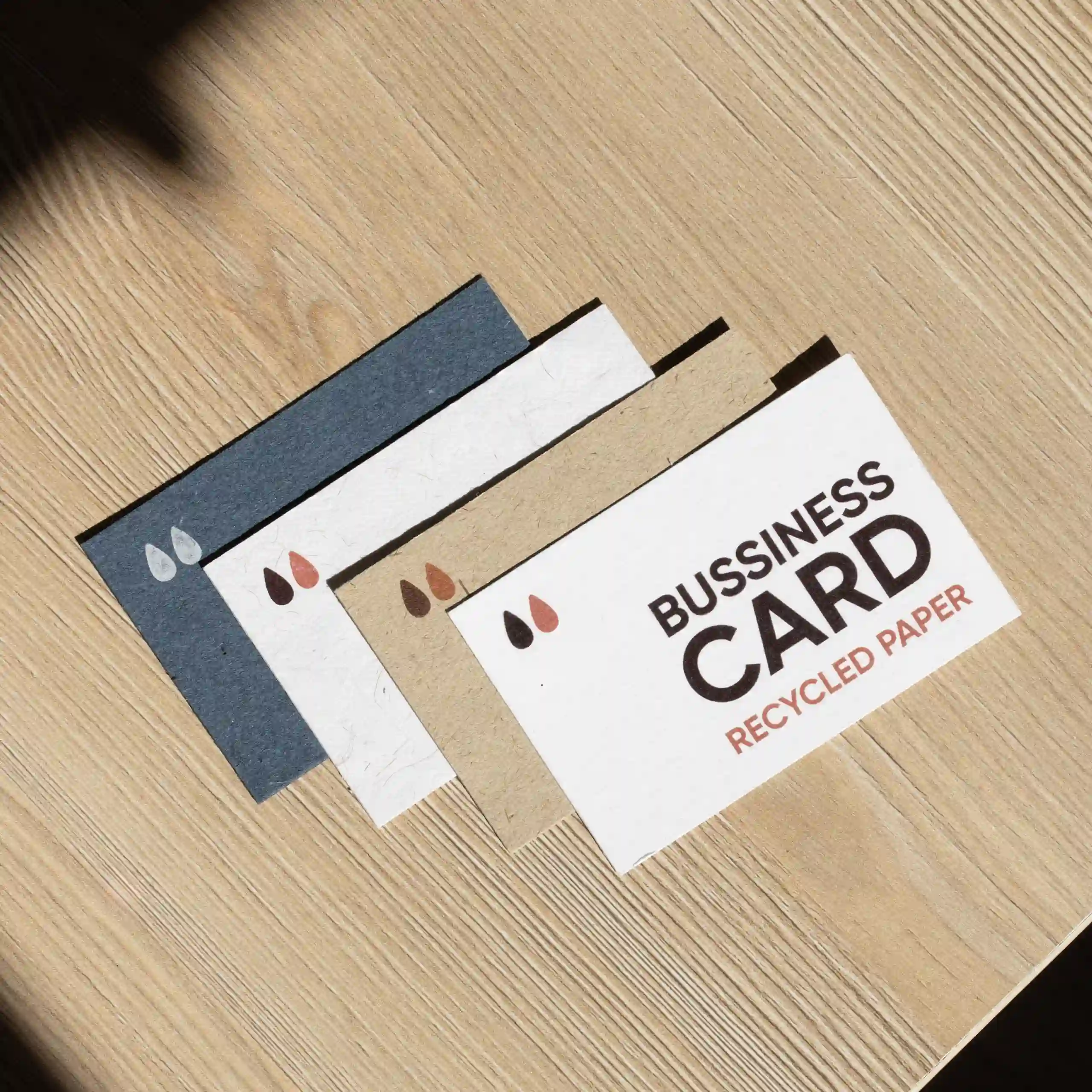 Cuatro tarjetas de visita impresas en papeles ecológicos sobre una superficie de madera