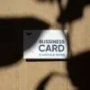 Tarjeta de visita impresa en papel plantable sobre una superficie de madera con sombras