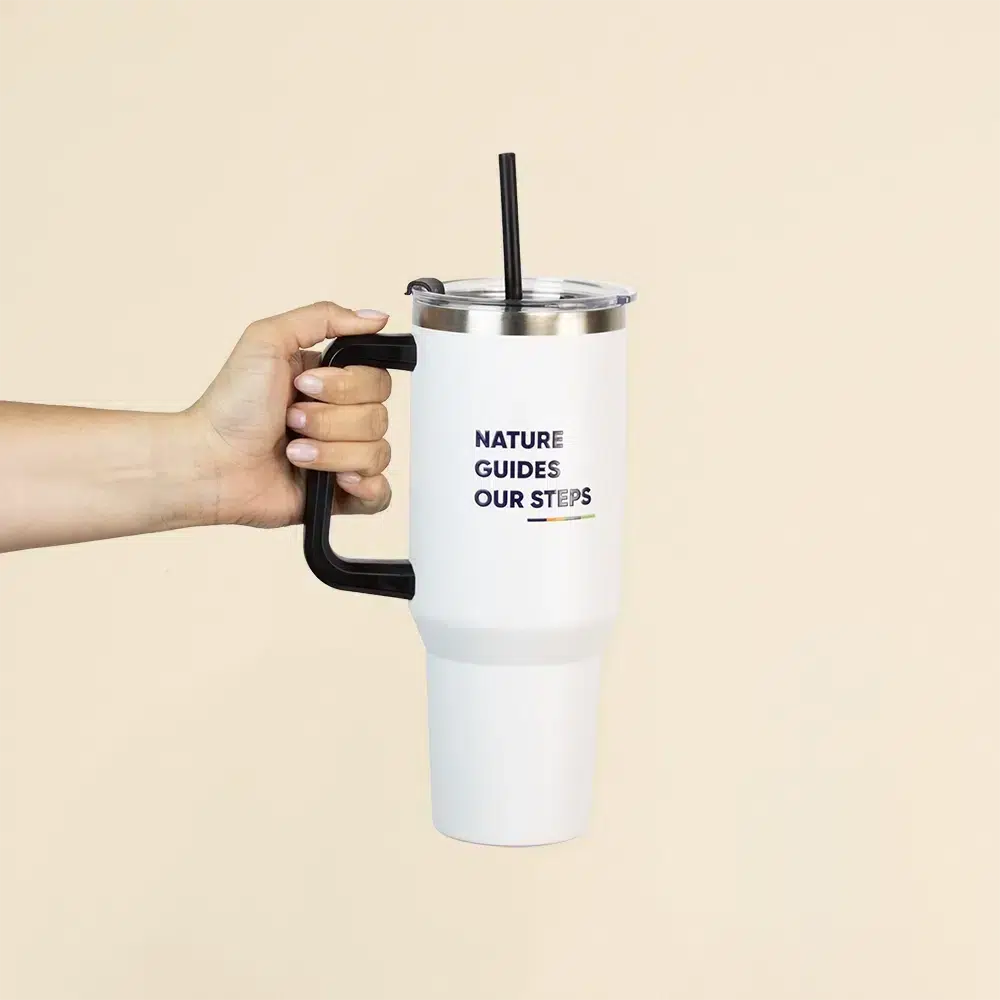 Mano sujetando un vaso térmico blanco personalizado de acero inoxidable con pajita sobre un fondo beige