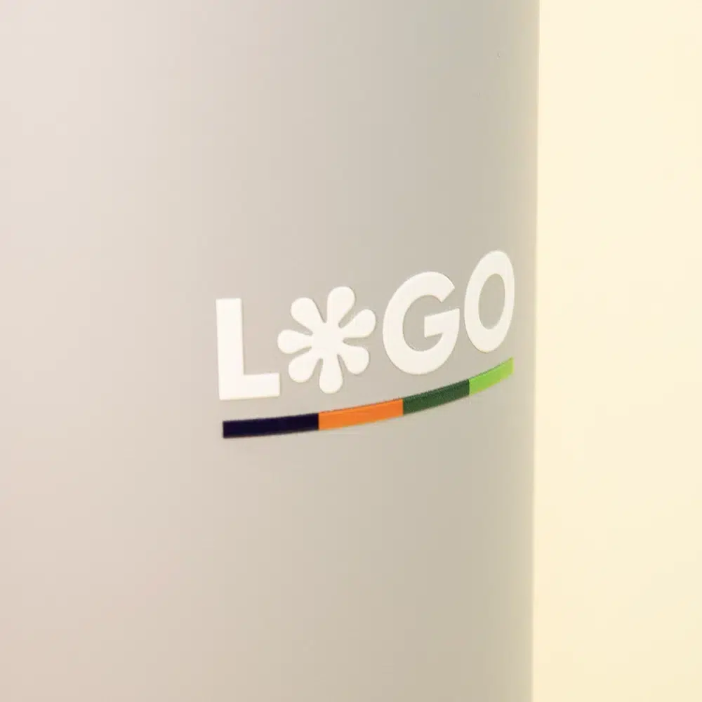 Primer plano de vaso térmico gris de acero inoxidable con logo sobre un fondo beige