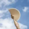 Abanico de madera personalizado FANI Mano sujetando un abanico de madera y algodón con el cielo de fondo