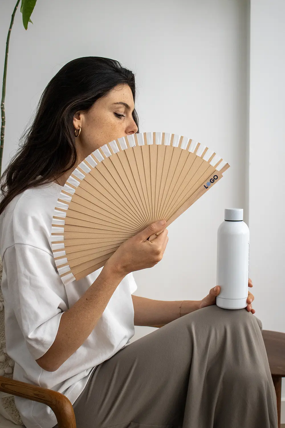 Chica de perfil sujetando un abanico de madera y algodón junto con una botella blanca