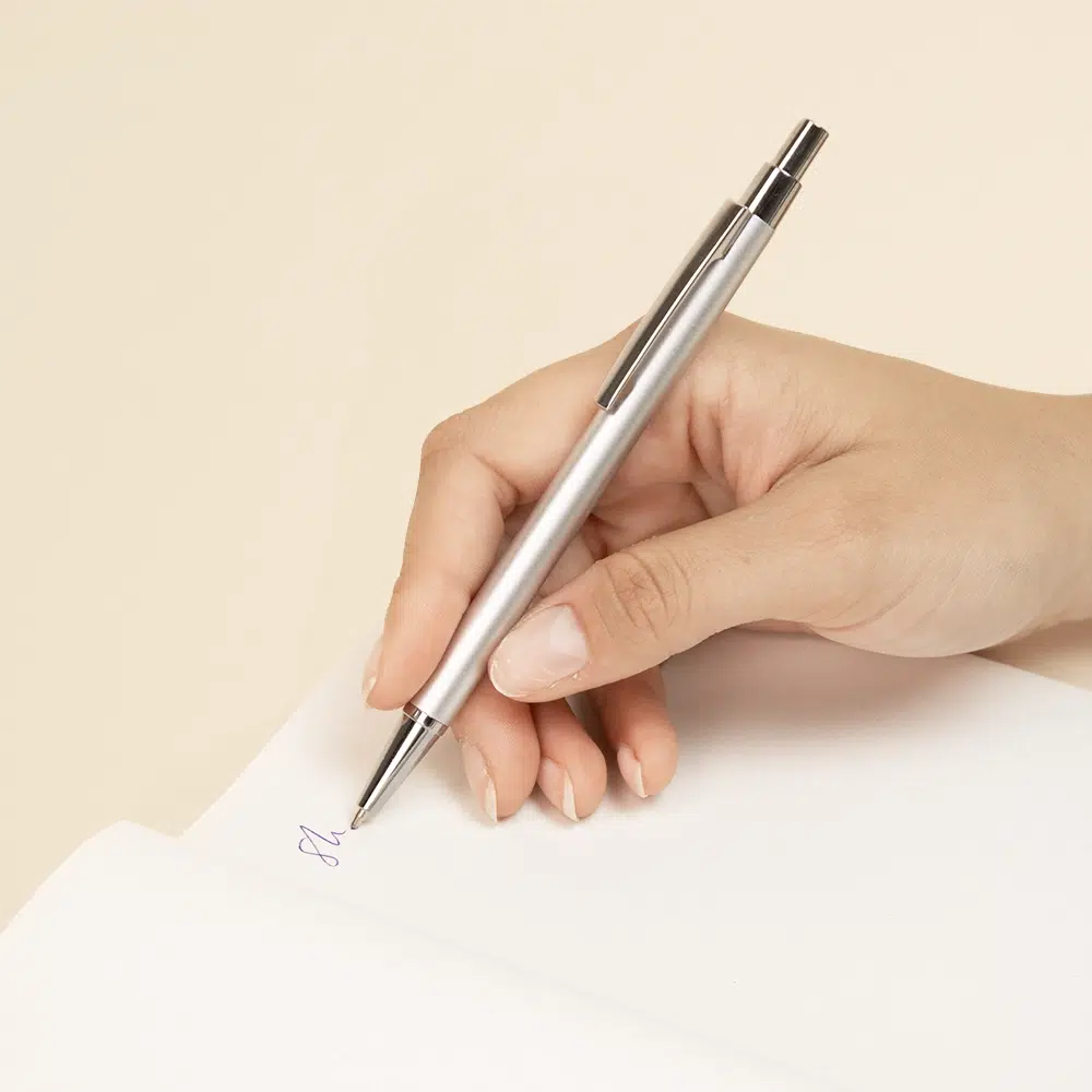 Bolígrafo de aluminio reciclado GANTE Mano escribiendo sobre un cuaderno con un bolígrafo plateado de aluminio reciclado