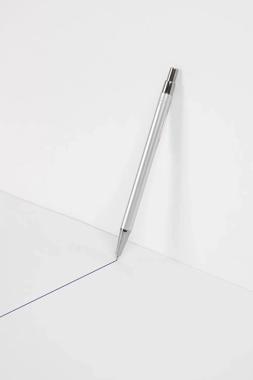 Un bolígrafo plateado de aluminio reciclado trazando una línea azul sobre una superficie blanca