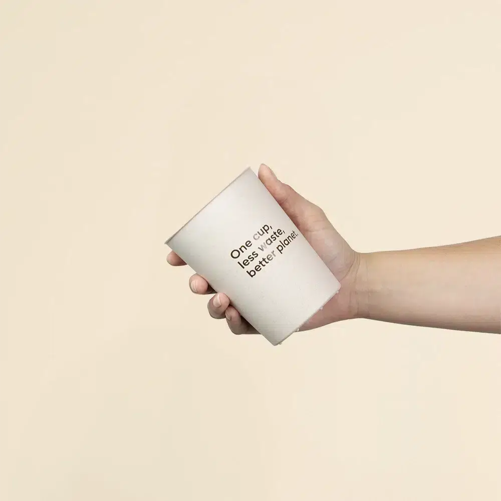 Mano sujetando vaso reutilizable de cáscara de arroz sobre un fondo beige