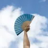 Mano sujetando un abanico azul con varillas de madera y tela poliester abierto con el cielo de fondo