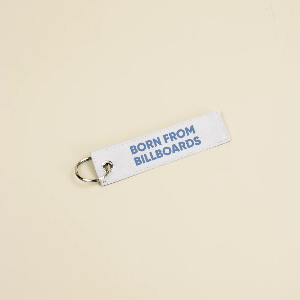 Llavero hecho con lona reciclada blanca personalizado con el texto impreso en azul: "Born from billboards"